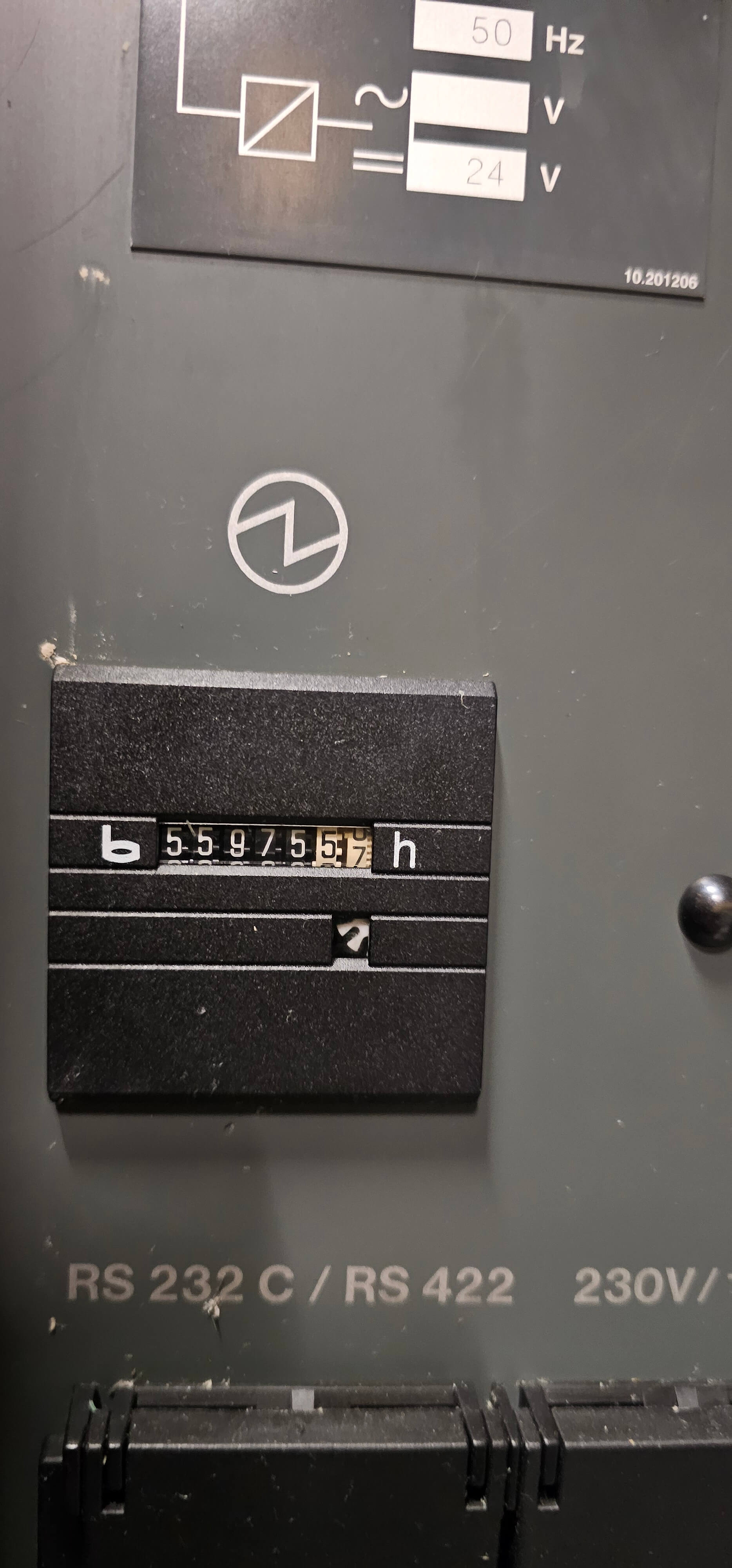 Nahaufnahme eines Stundenzählers mit der Anzeige 55975 Stunden. Zu sehen sind auch technische Angaben wie RS 232 C/RS 422 und 230V.